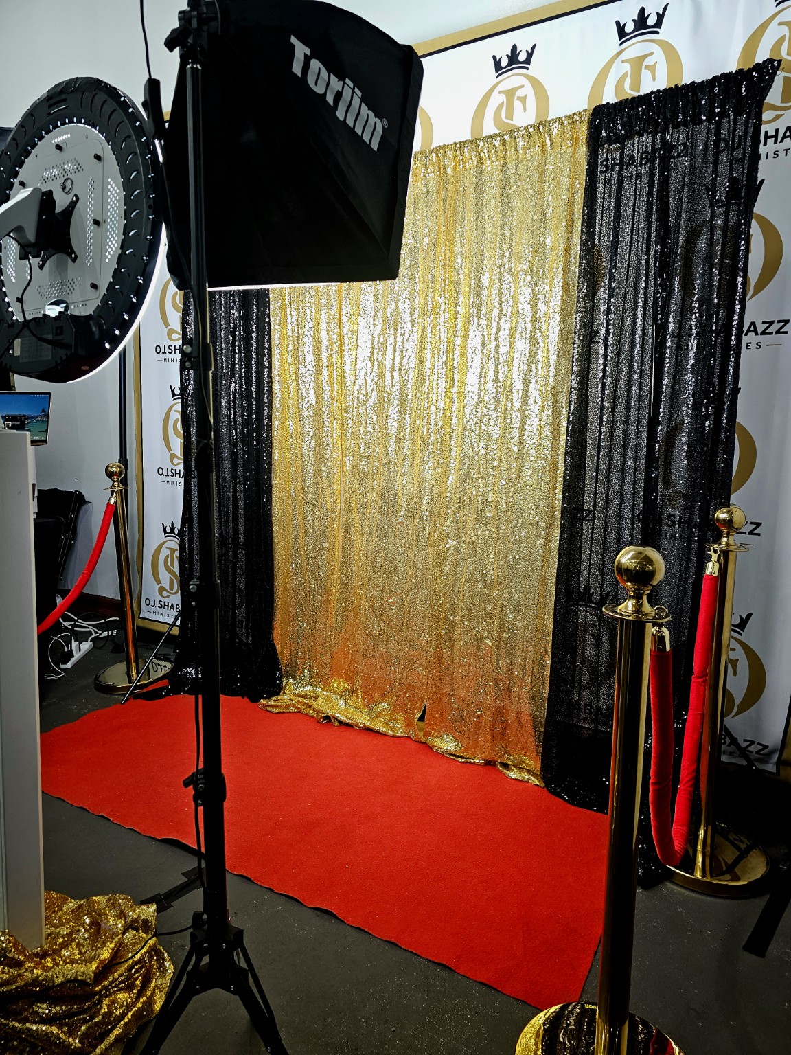 Black-and-gold sequin backdrop with red carpet, gold stanchions and photo booth lighting
