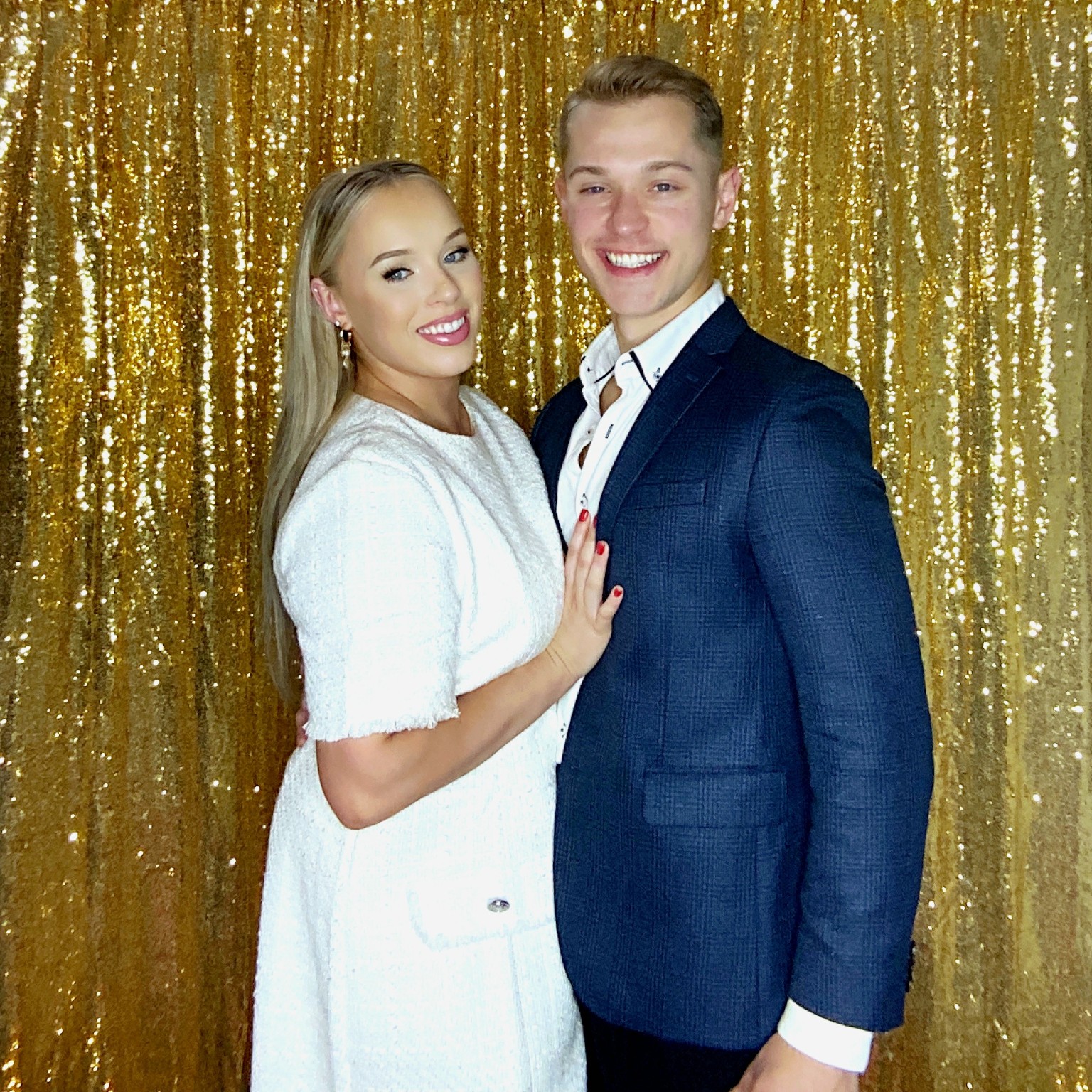 Newlyweds posing in front of a gold sequin photo booth backdrop